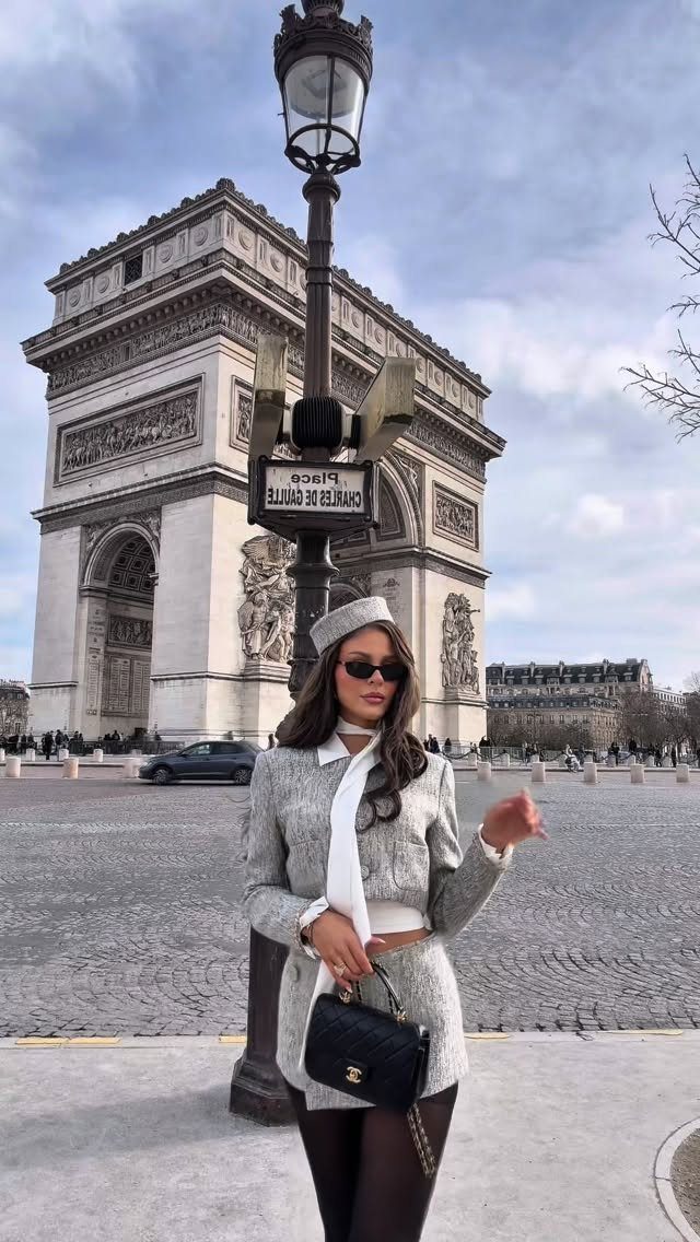 Woman in grey tweed suit and beret posing before the Arc de Triomphe.