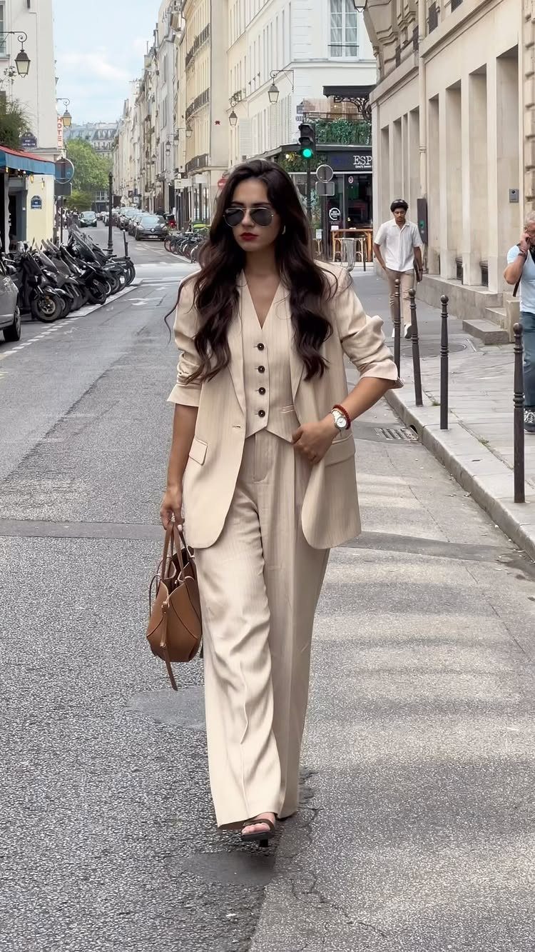 Woman in a beige waistcoat and tailored trousers walking on a city street.
