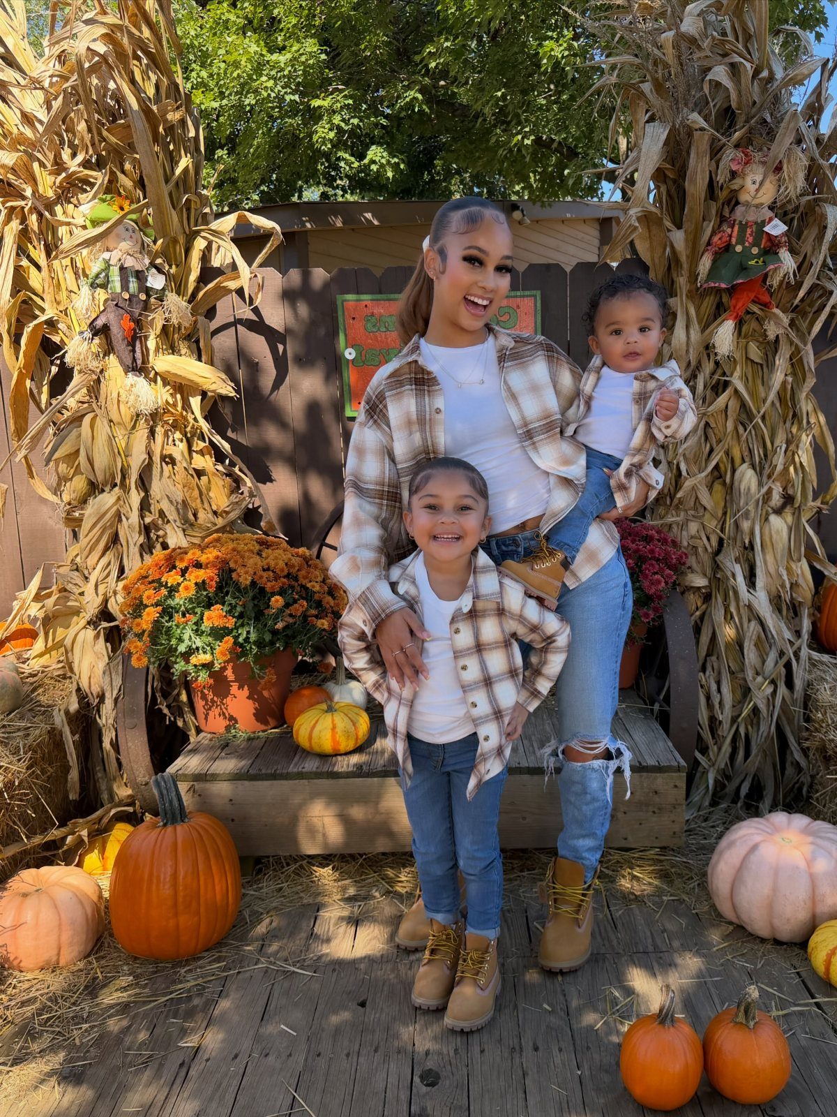 Woman and two children in matching plaid shirts and jeans at a pumpkin patch