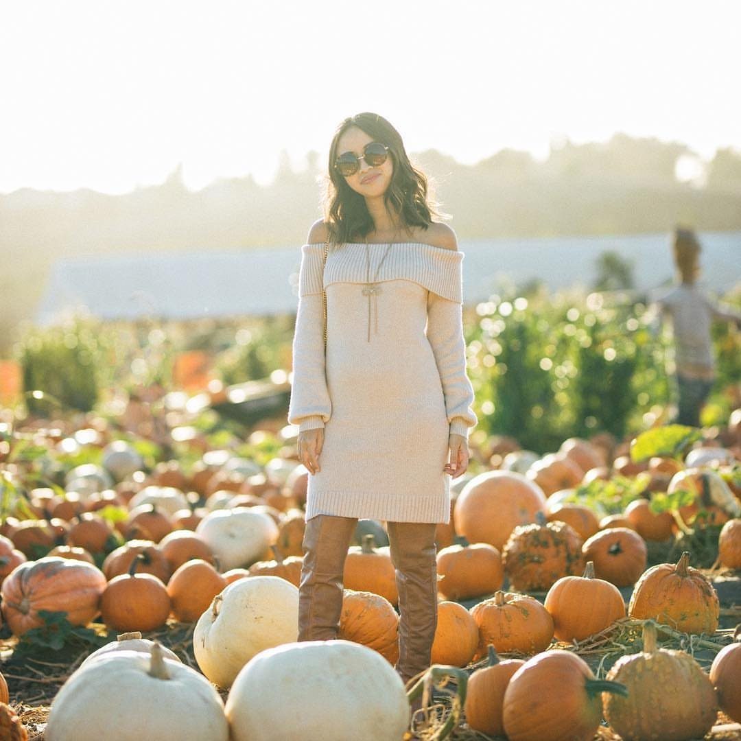 Woman in cream sweater dress and brown boots standing in pumpkin patch