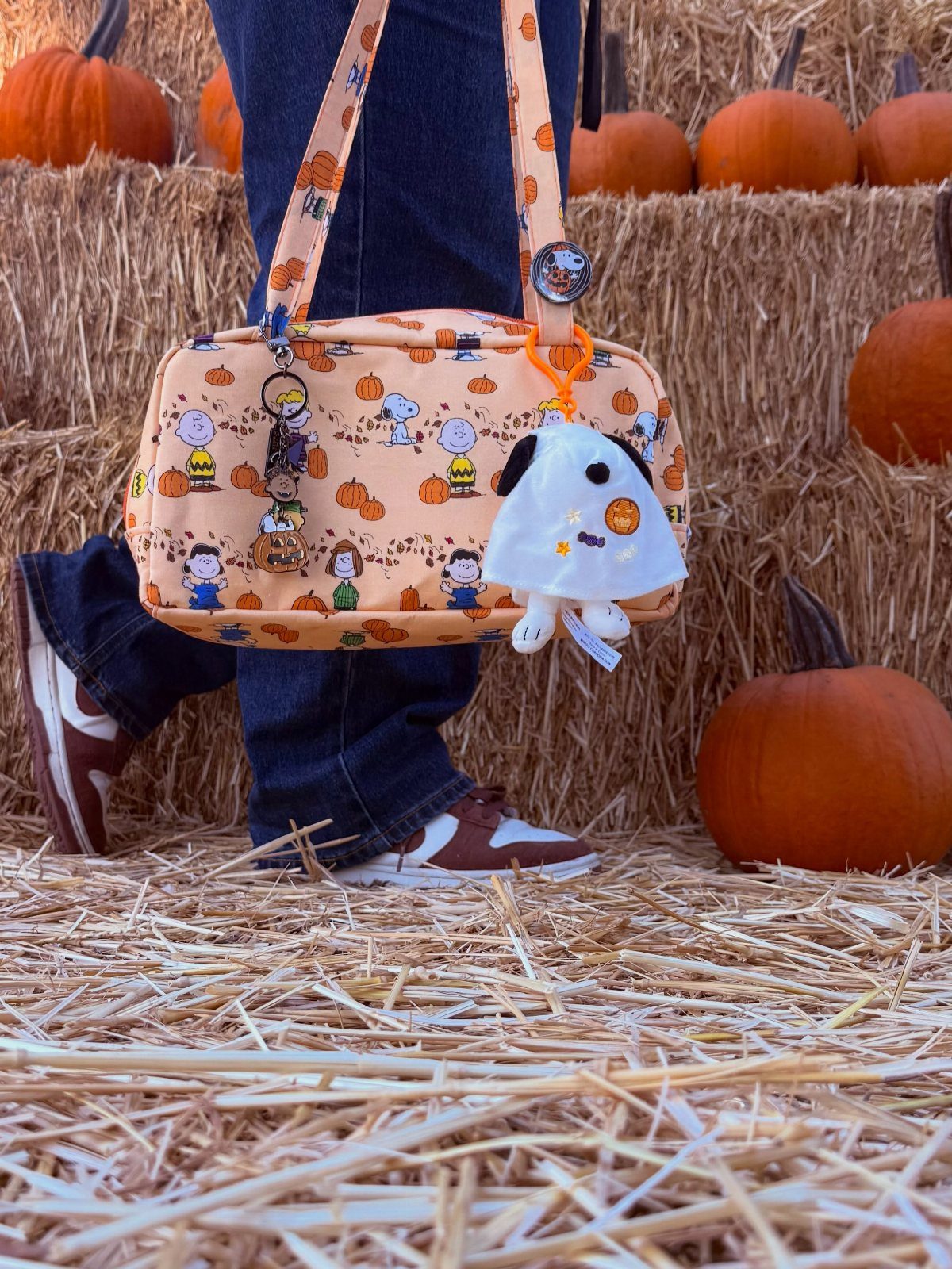 Orange Peanuts character crossbody bag worn by person in a pumpkin patch