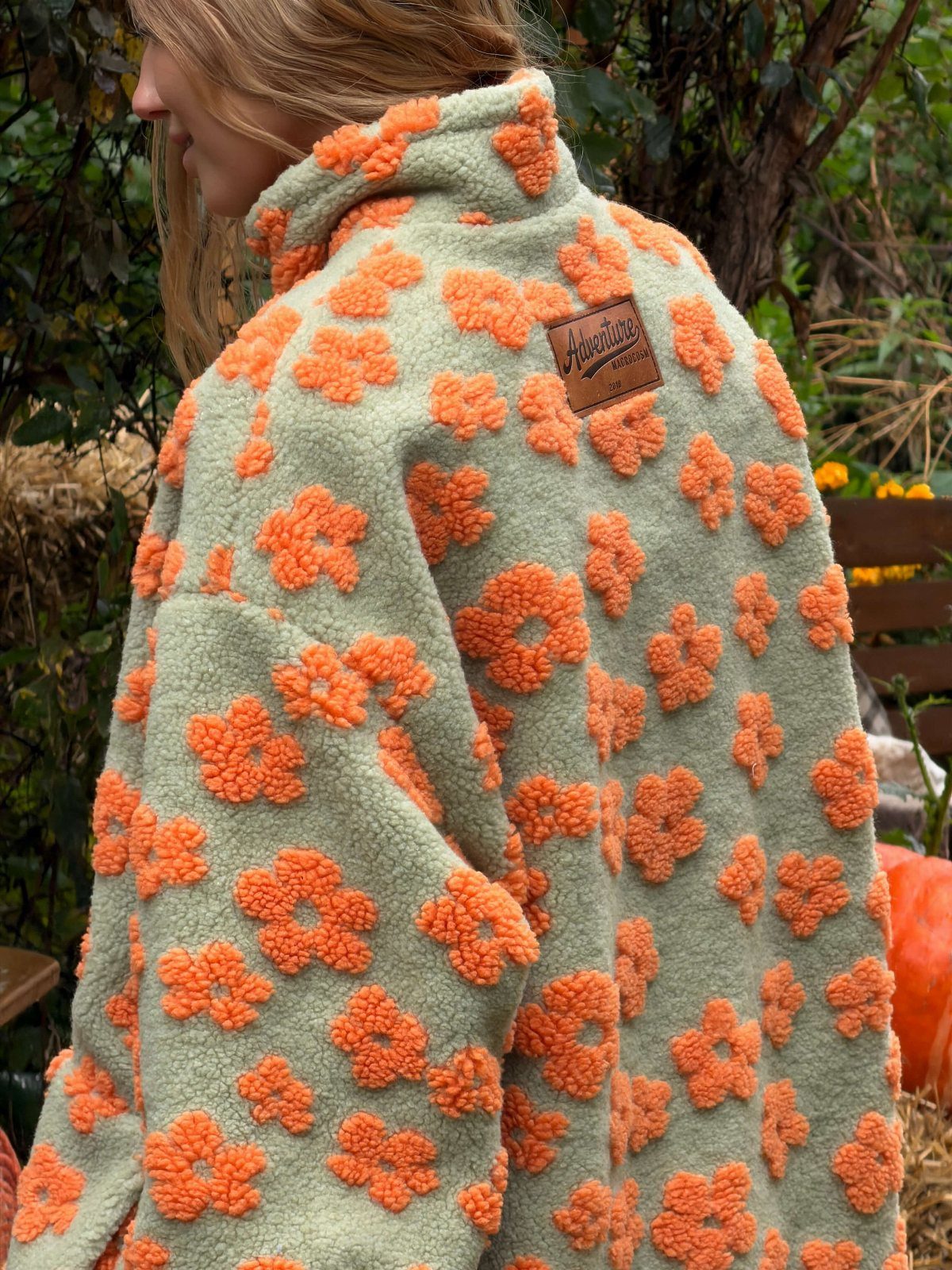 Woman wearing a sage green fleece jacket with orange flowers in a garden