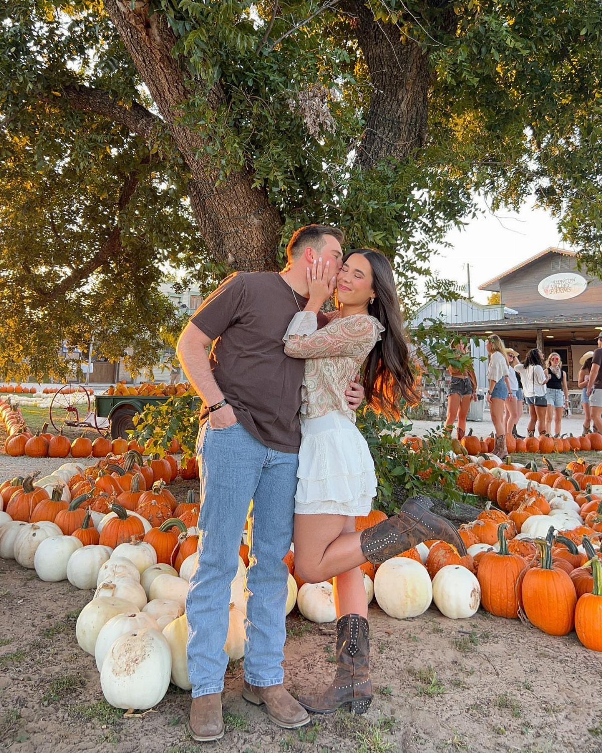 Couple posing in a pumpkin patch, man wearing blue jeans and brown boots.