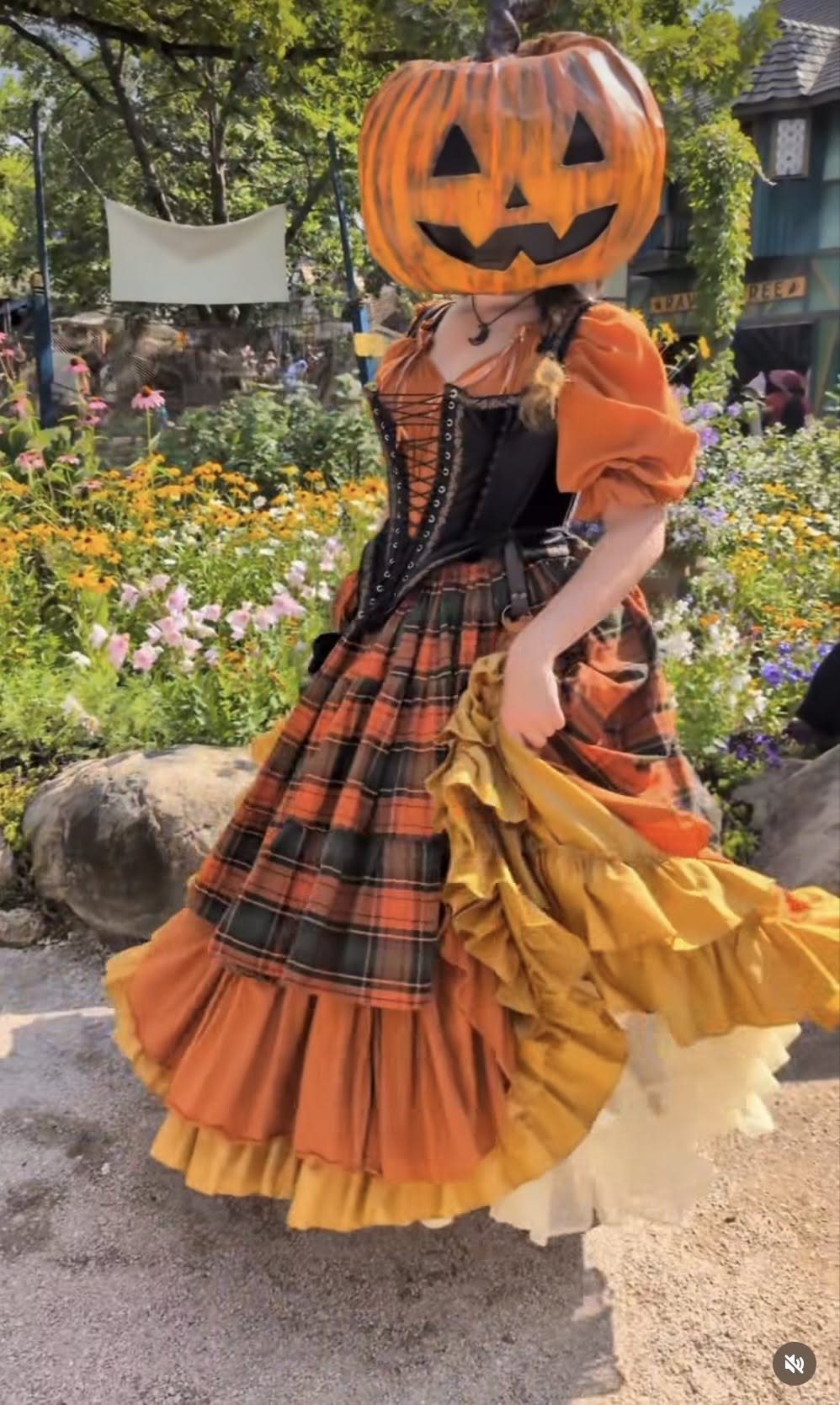 Person in pumpkin mask wearing orange plaid dress with black corset and ruffles