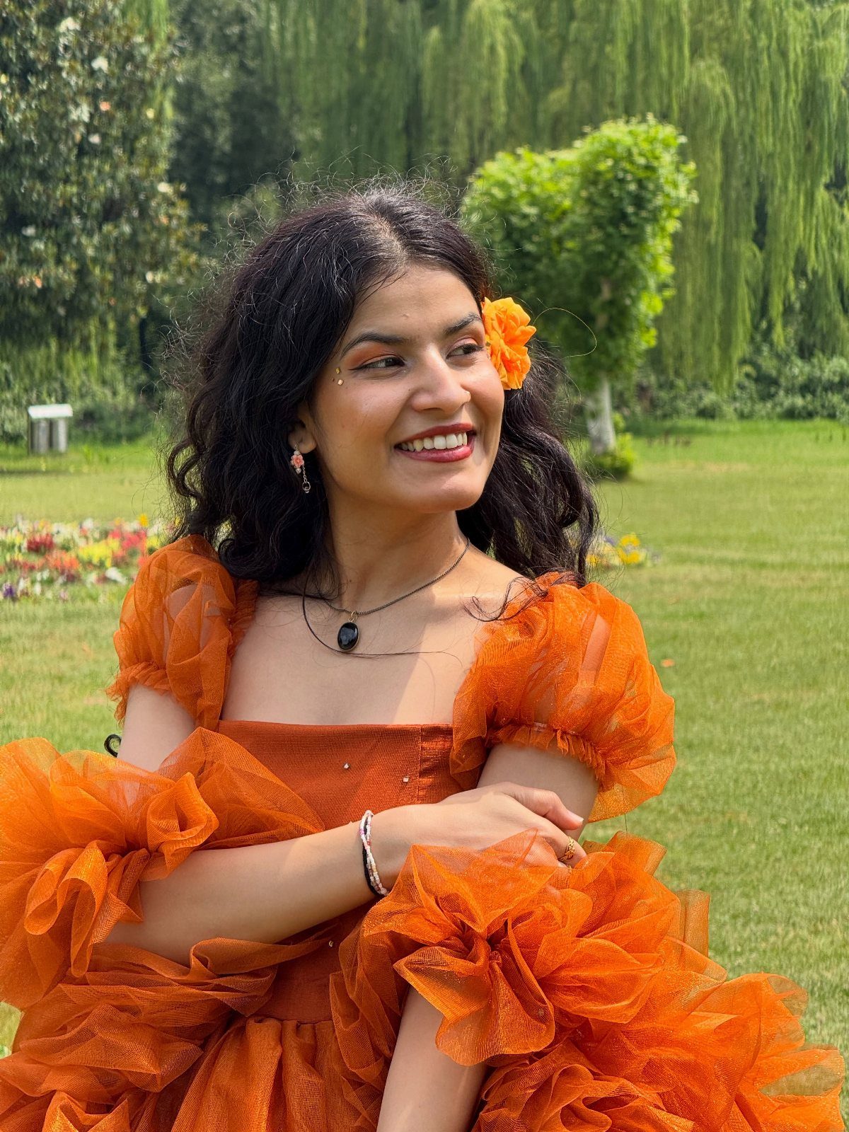 Woman in a bright orange tulle dress sitting in a green park.