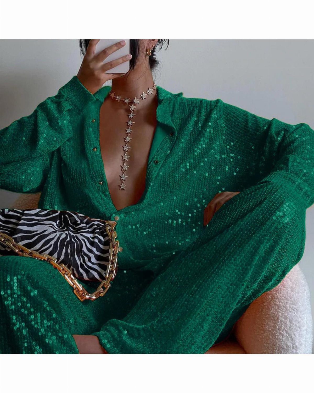 Person wearing an emerald green sequin outfit with a star necklace and zebra clutch