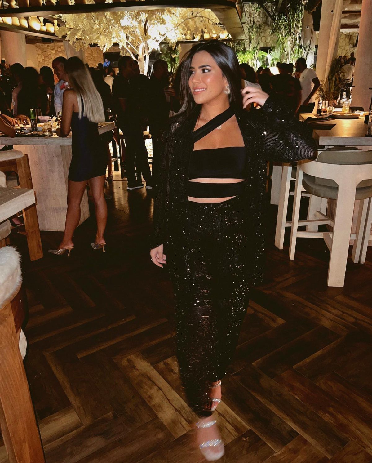 Woman in a black sequin suit and crop top posing in a restaurant.