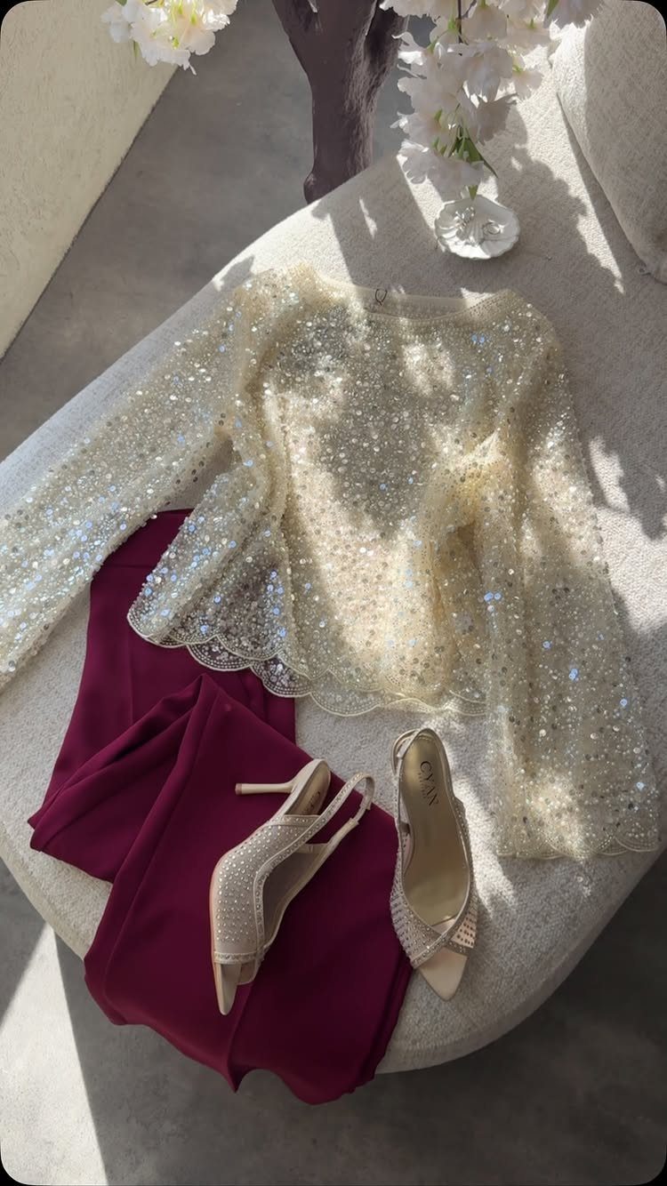 Gold sequined top, burgundy pants, and gold heels arranged on a light ottoman.