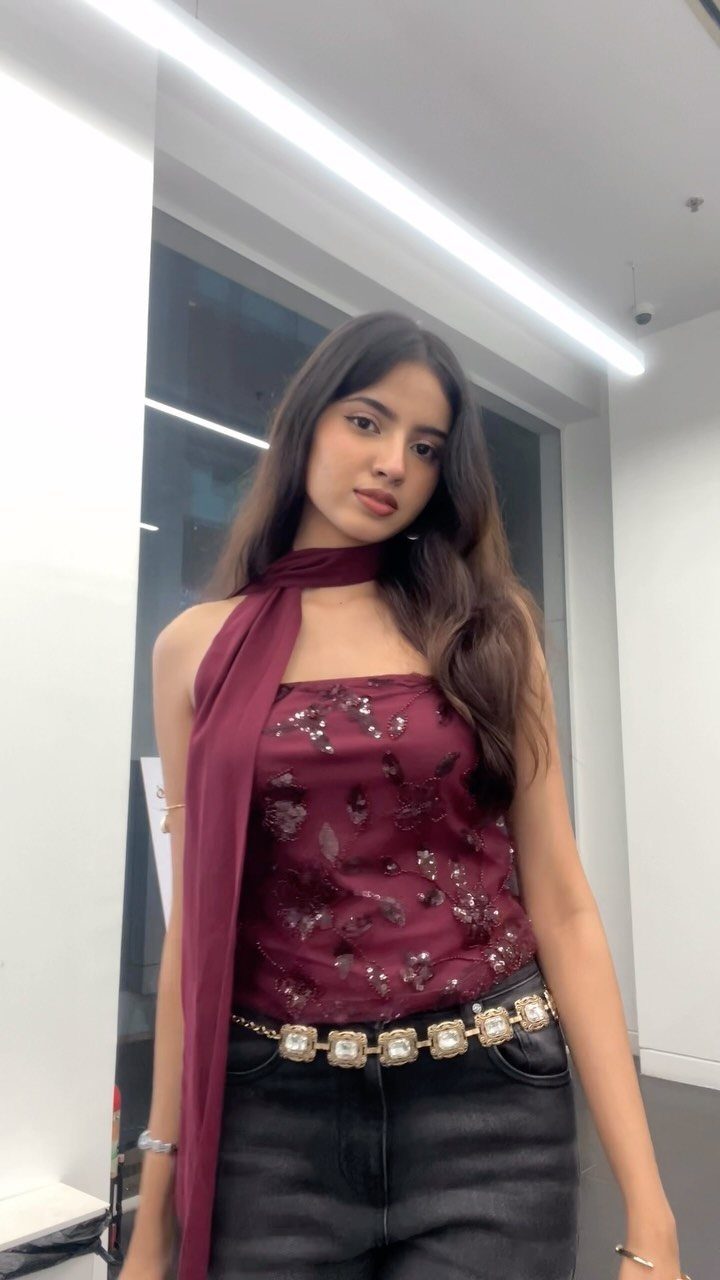 Woman wearing a maroon sequined top, matching scarf, and crystal chain belt.