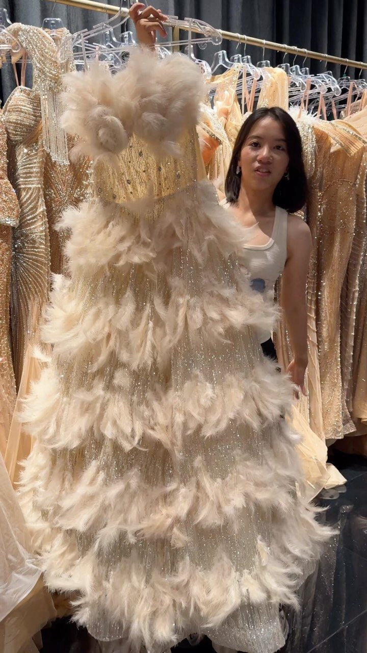 Champagne feather dress with sequined bodice held up by a woman in a boutique.