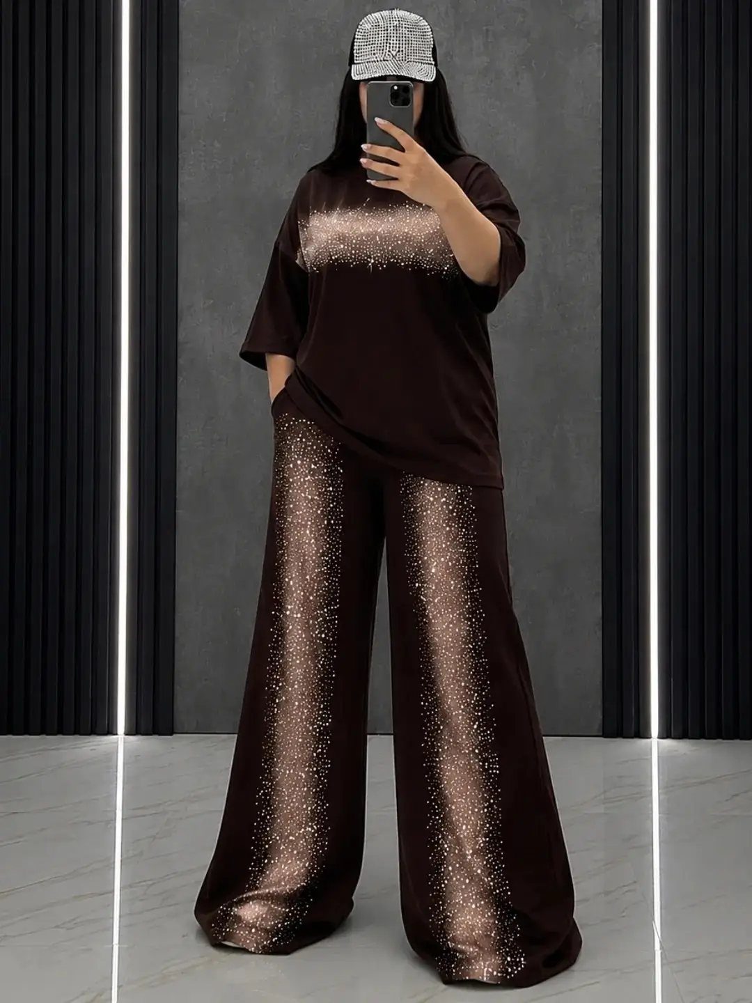 Person in brown glittery top and wide-leg trousers wearing a silver sequined cap.