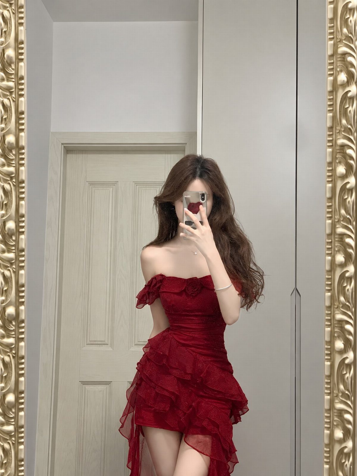 Woman in a ruffled red strapless dress taking a mirror selfie in a room.