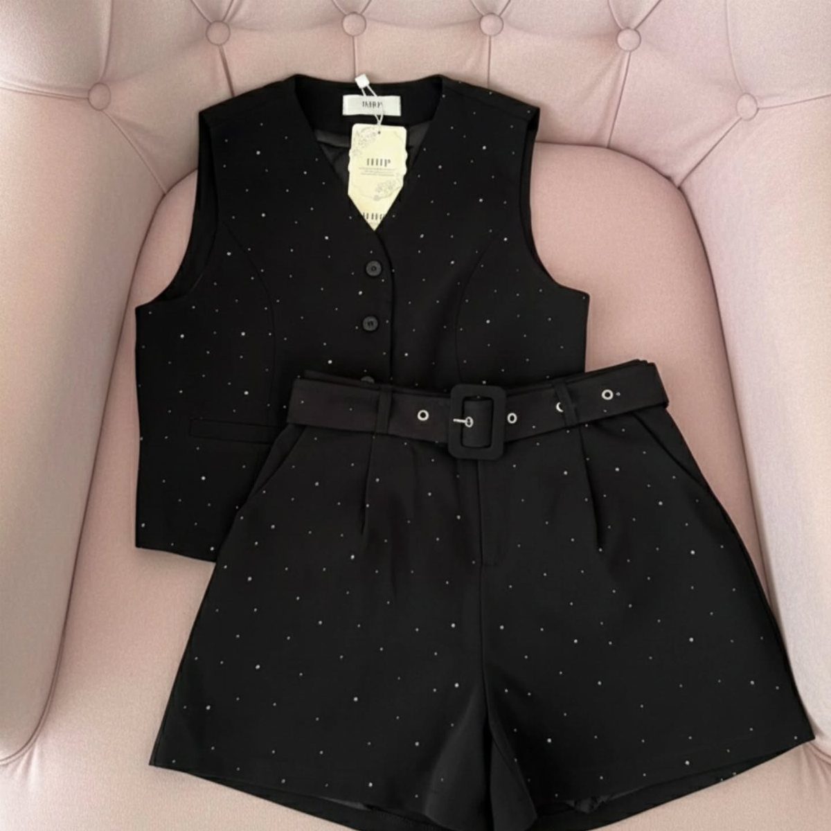 Black sparkly sleeveless blazer and matching shorts set on a pink tufted chair
