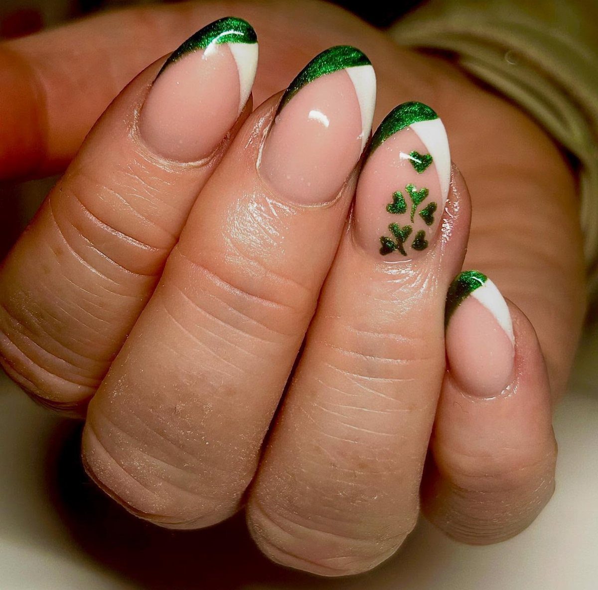 Almond shaped nails with green glitter French tips and small green shamrock designs.