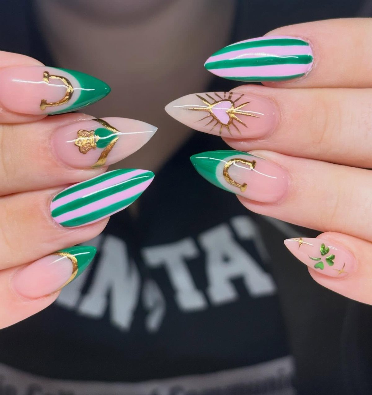 Almond-shaped nails with green and pink stripes and gold St Patrick's Day accents.