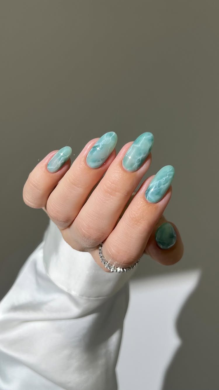 Almond nails with pastel green and white marble art and a diamond ring.