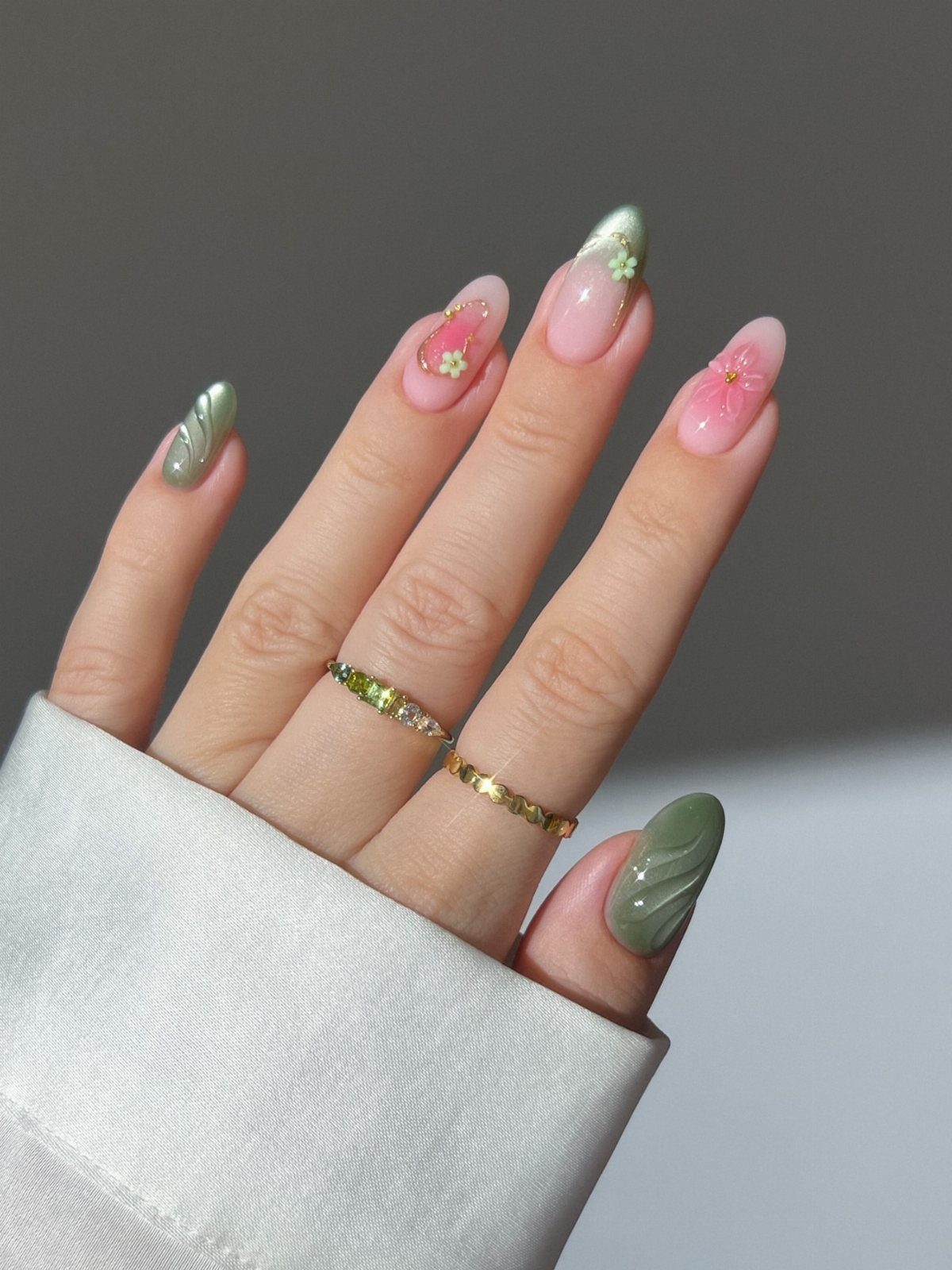 Almond nails with sage green and pink floral designs and gold rings.