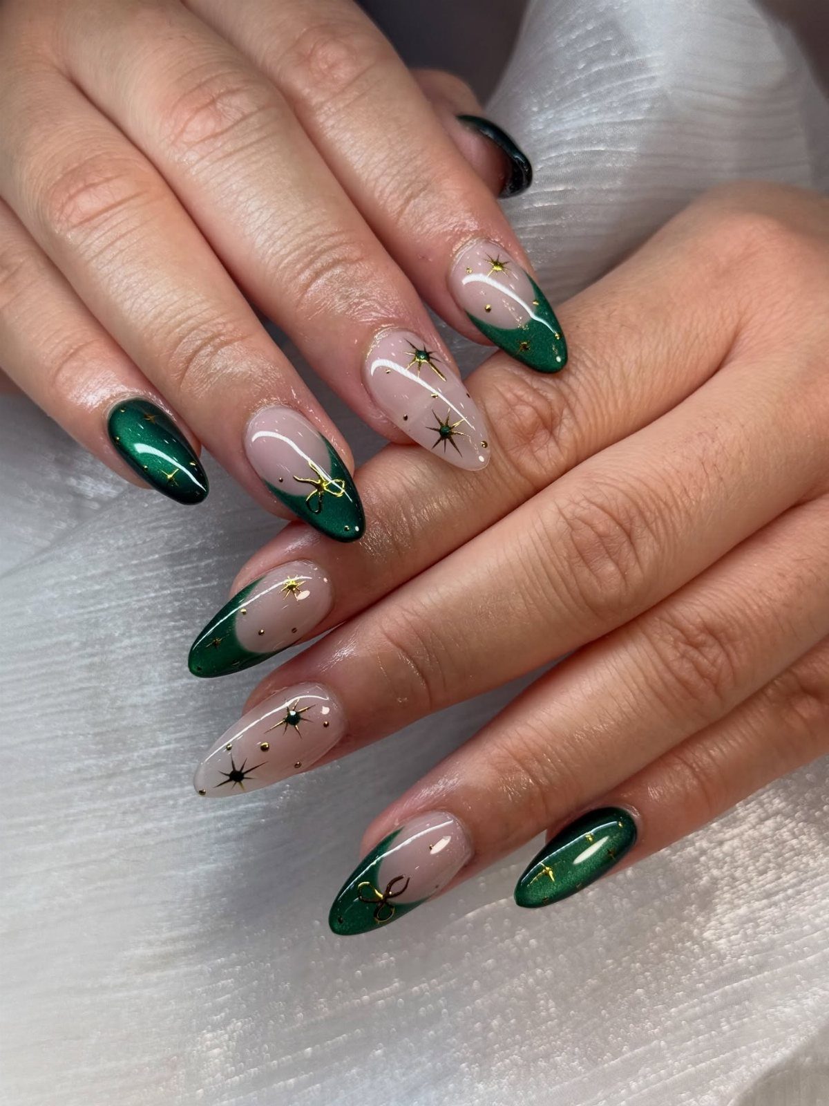 Almond shaped nails with emerald green polish and gold star foil accents.