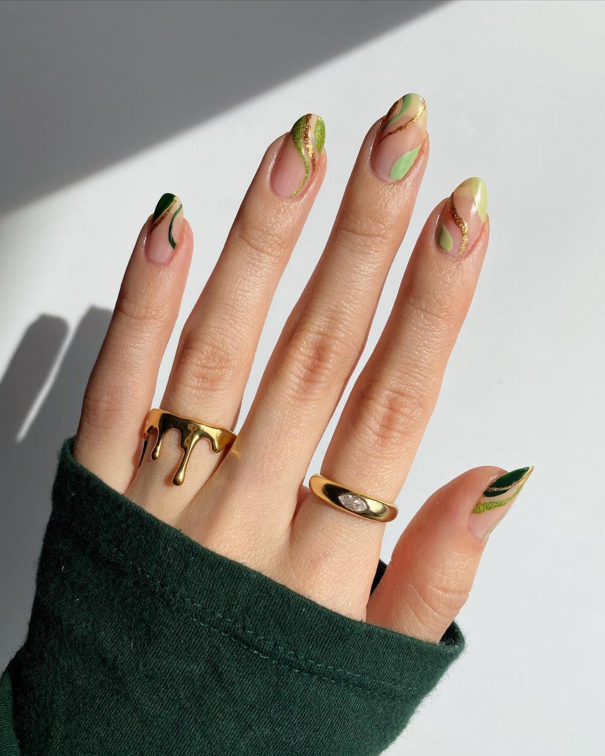 Hand with almond nails featuring abstract green swirls and gold foil accents.