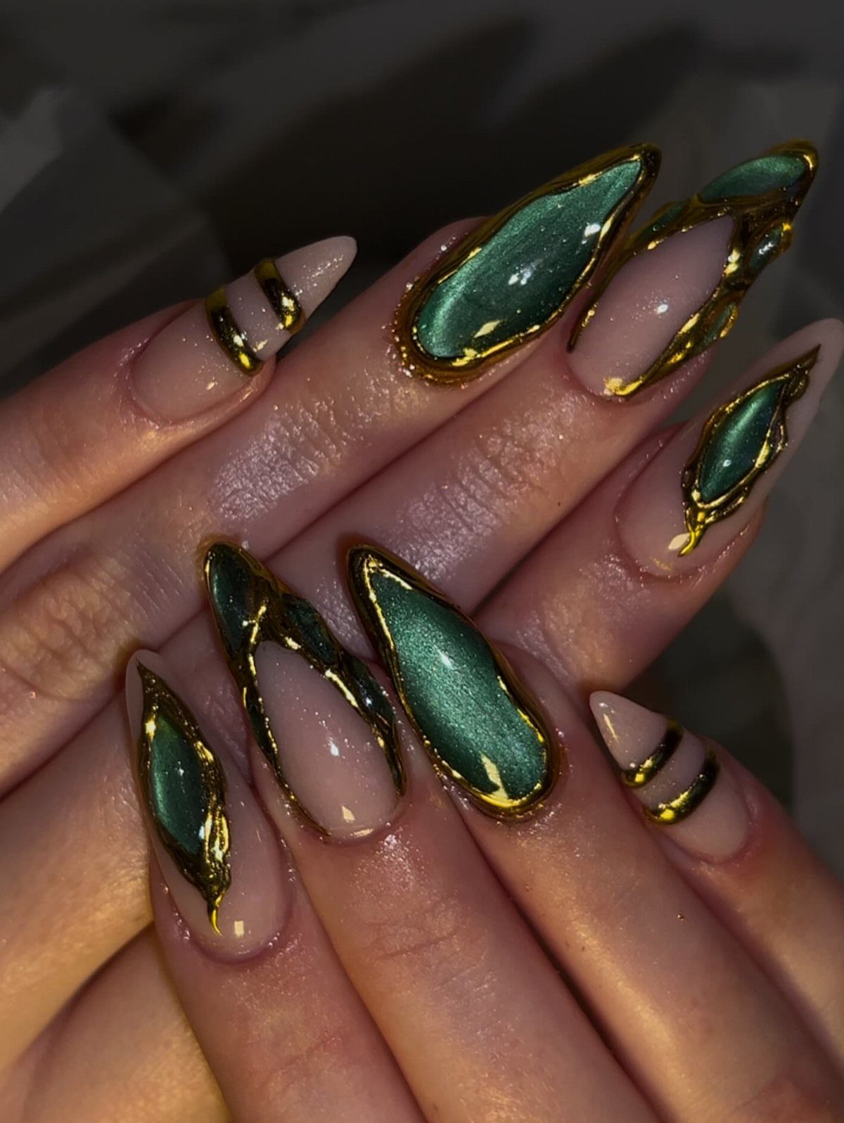 Almond nails with nude base, emerald green chrome accents, and metallic gold outlines.