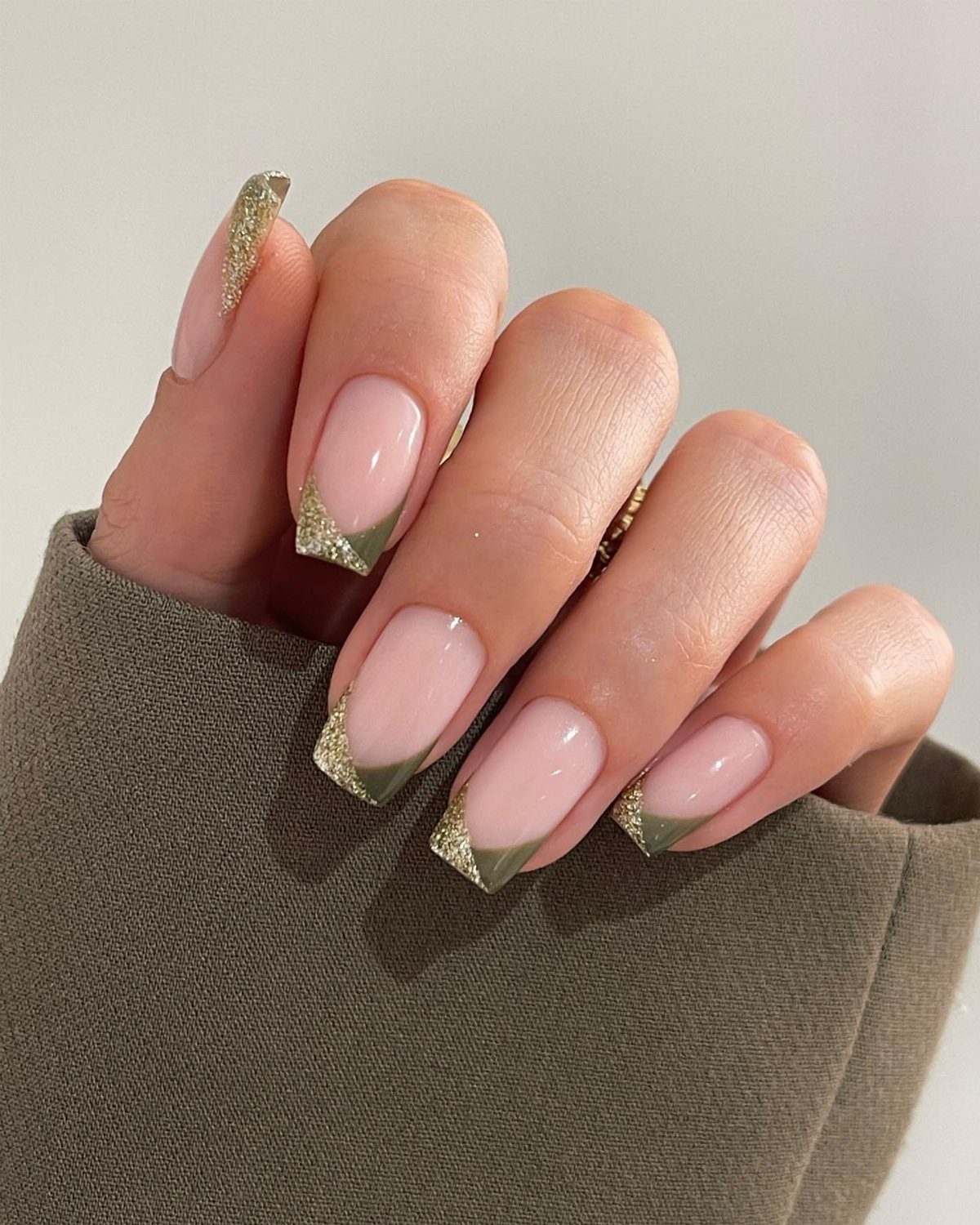 Almond nails with nude base, olive green French tips and gold glitter accents.
