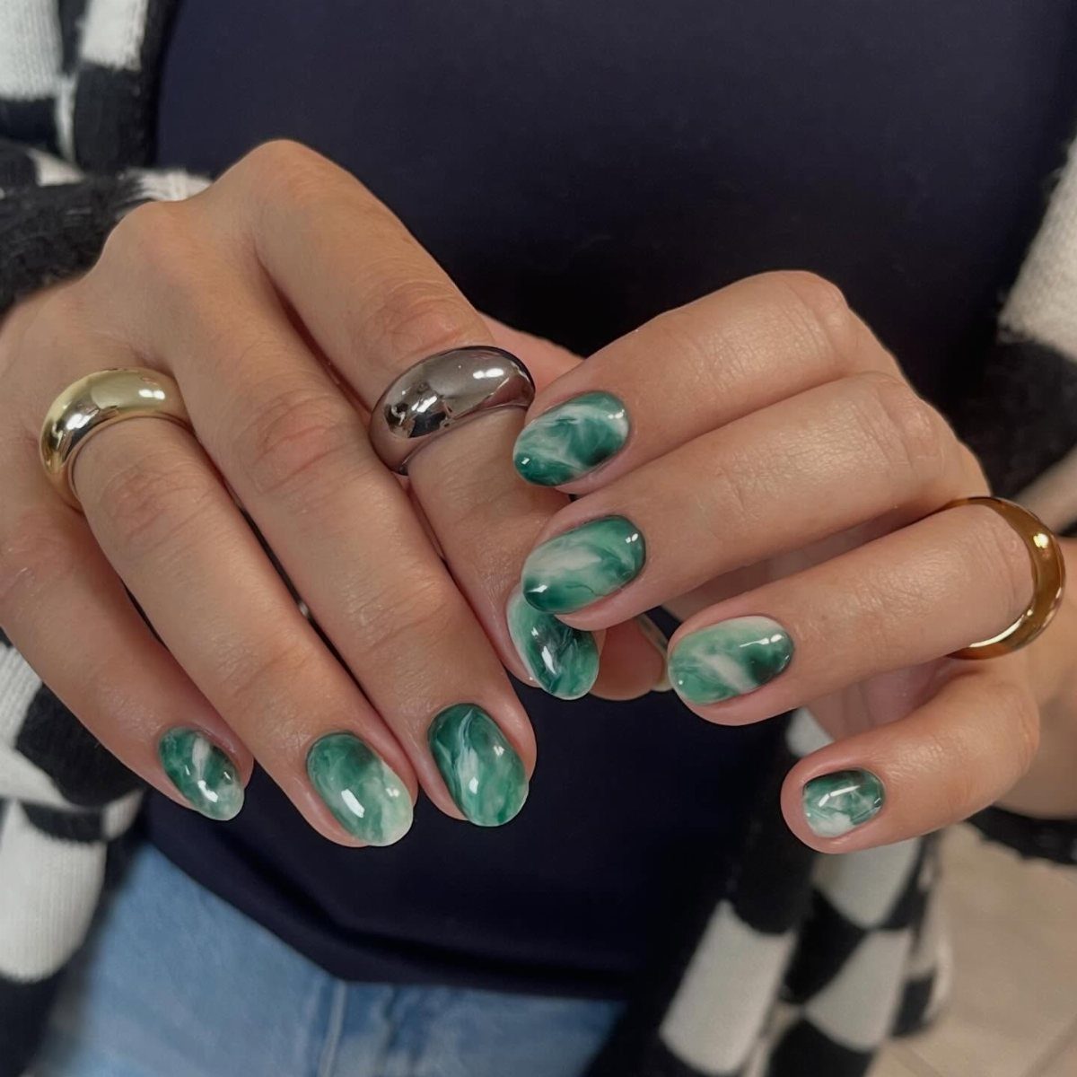Green and white marble nails on a person wearing gold and silver rings.