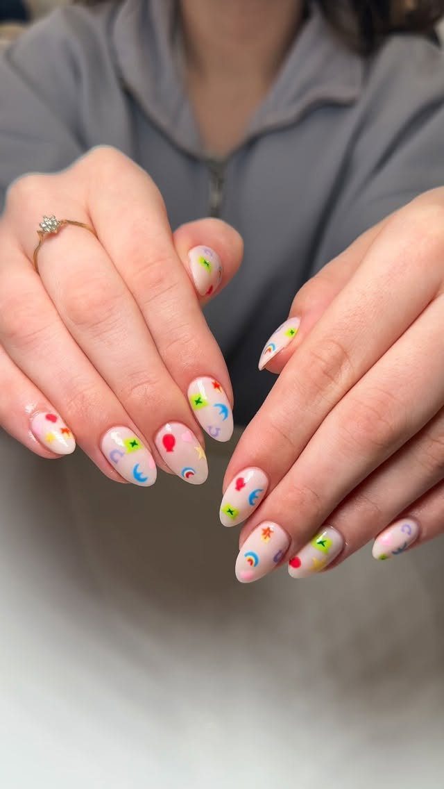 Almond-shaped nails with pink base and colorful lucky symbols like shamrocks and rainbows.