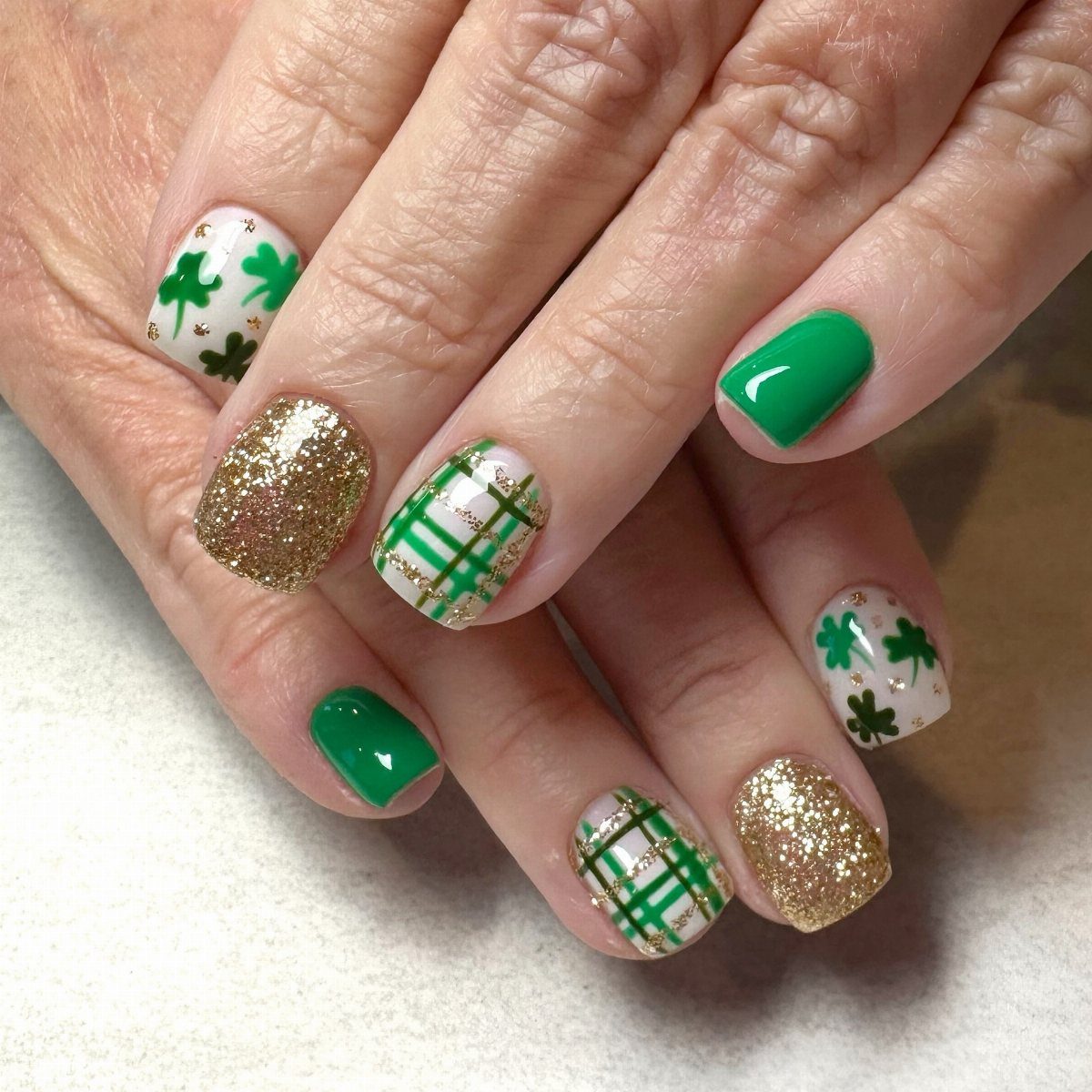 Manicured nails featuring green polish, gold glitter, shamrocks, and green plaid patterns.