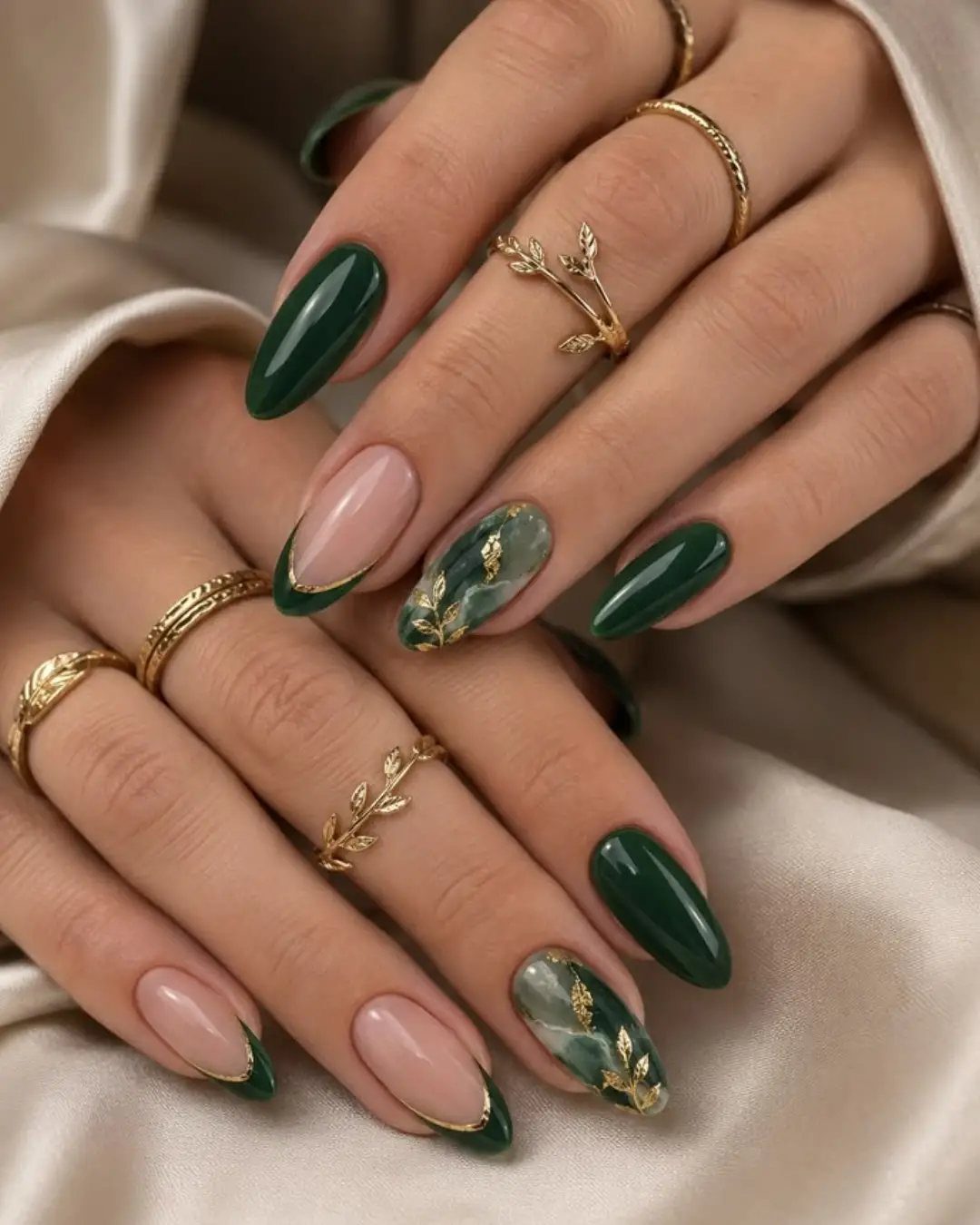 Almond nails featuring dark emerald green, nude tips, and green marble with gold foil.