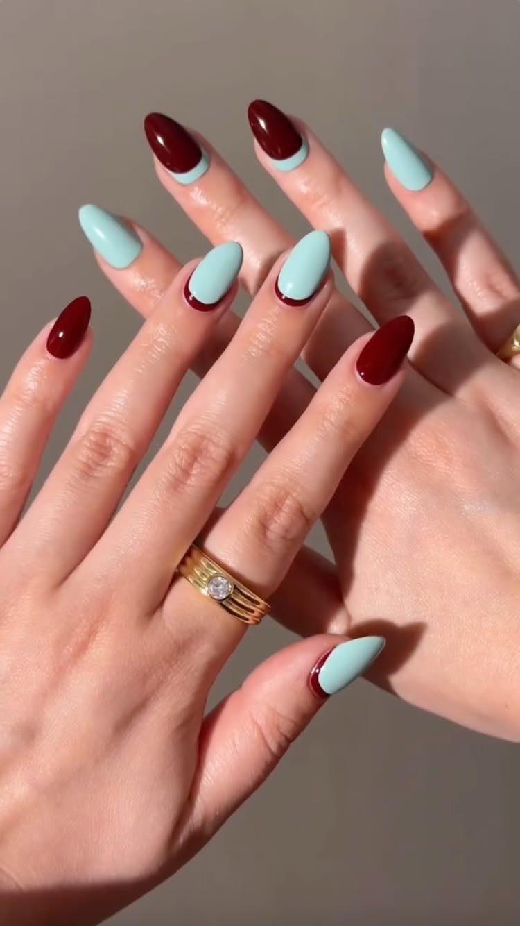 Almond-shaped nails painted in alternating deep red and light blue on two hands.