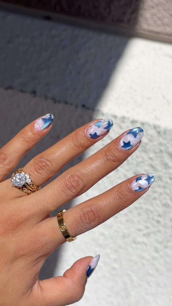 Manicured nails with blue stars and white clouds on a hand with gold rings.