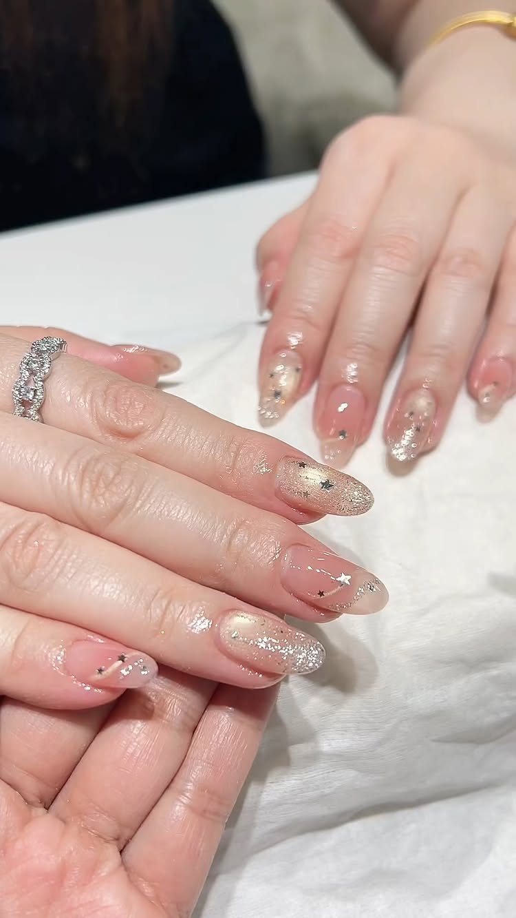 Oval nails with clear polish, silver glitter, and small gold and silver stars.