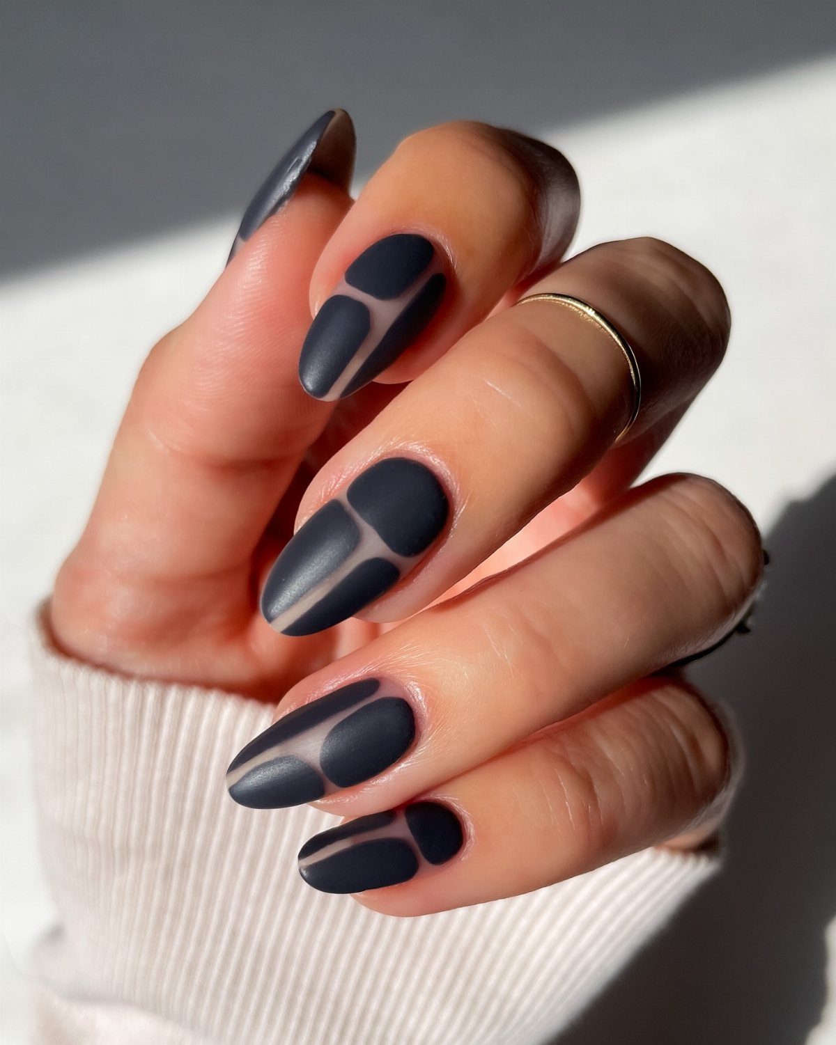 Matte navy blue almond nails with negative space curved line designs on a hand.