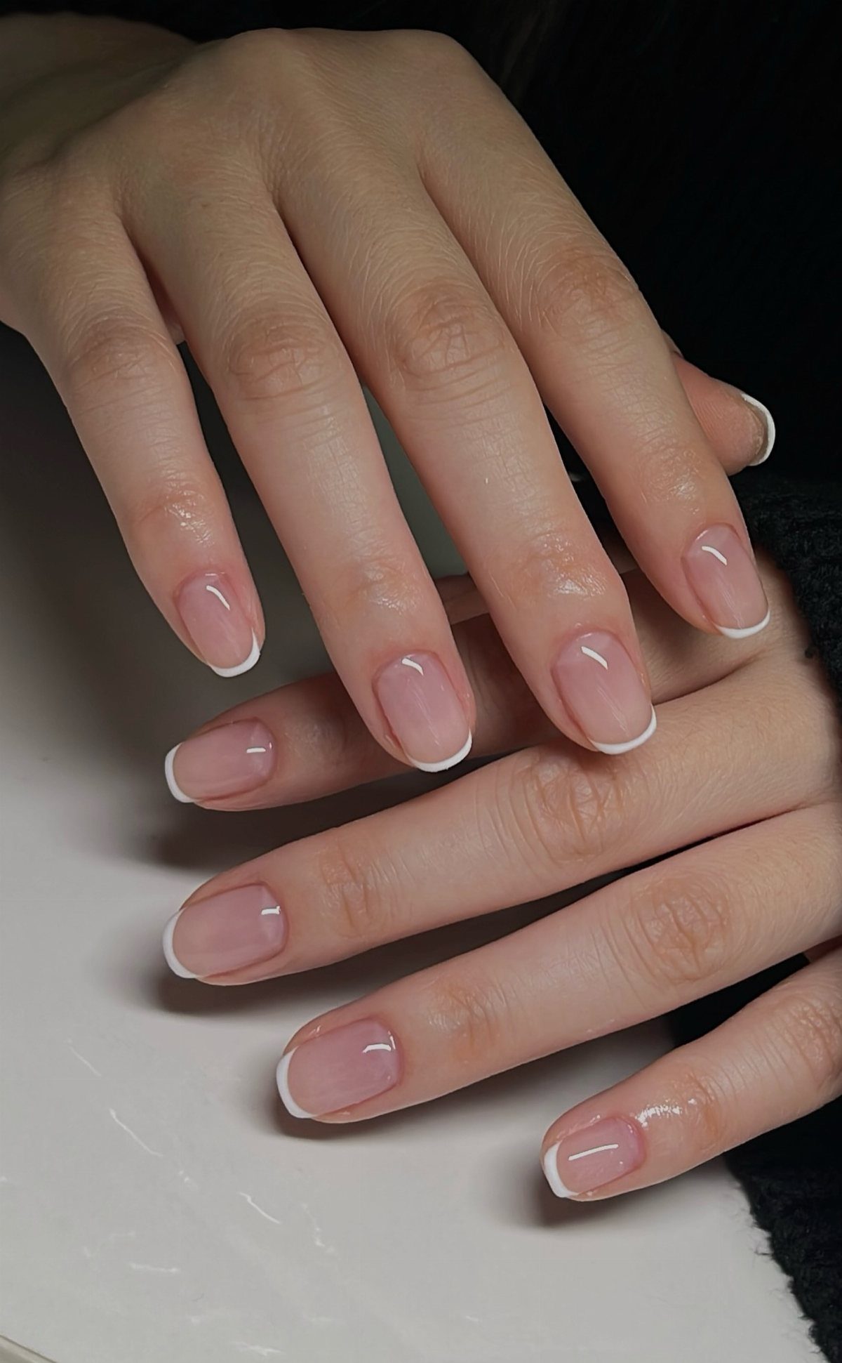 Manicured nails with thin white French tips on a natural glossy base.