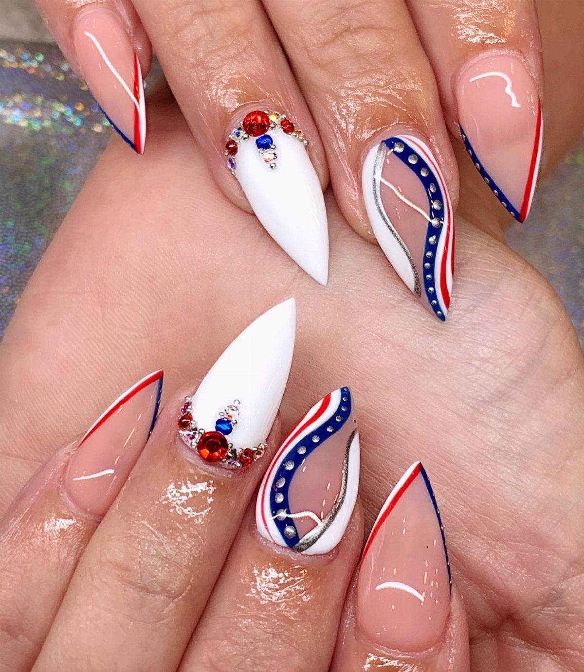 Pointed almond nails with red, white, and blue patriotic designs and gems.