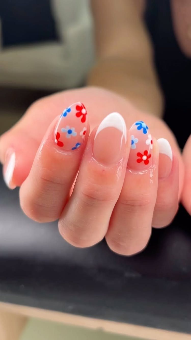 Manicured nails with white tips and small red and blue floral nail art.
