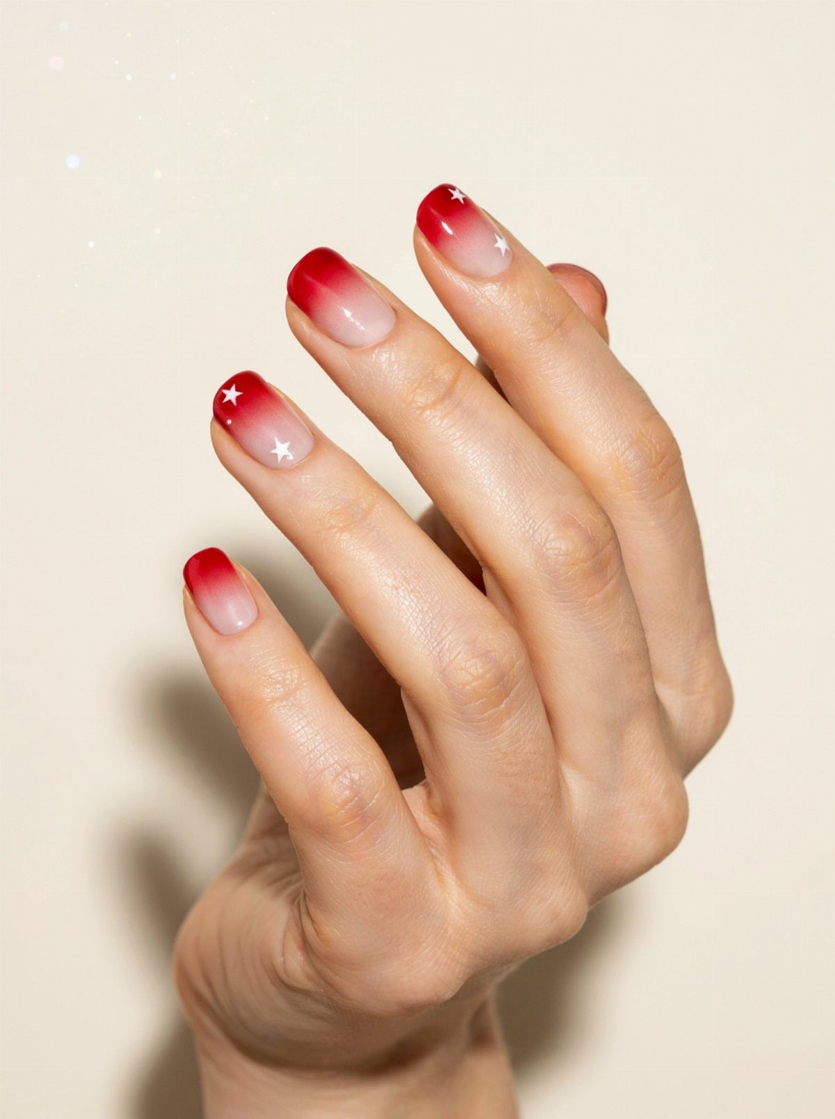 Hand with red and white ombre nails decorated with small white stars.