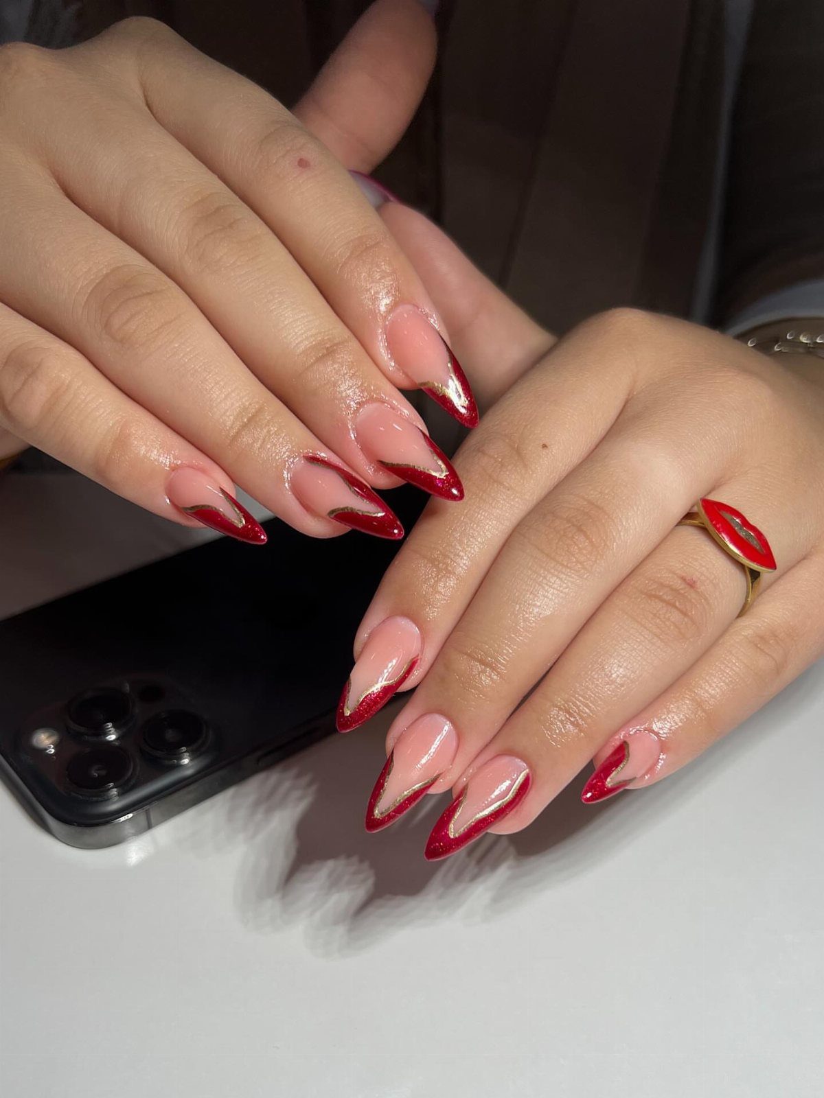 Almond-shaped nails with nude base and red V-shaped French tips on hands.