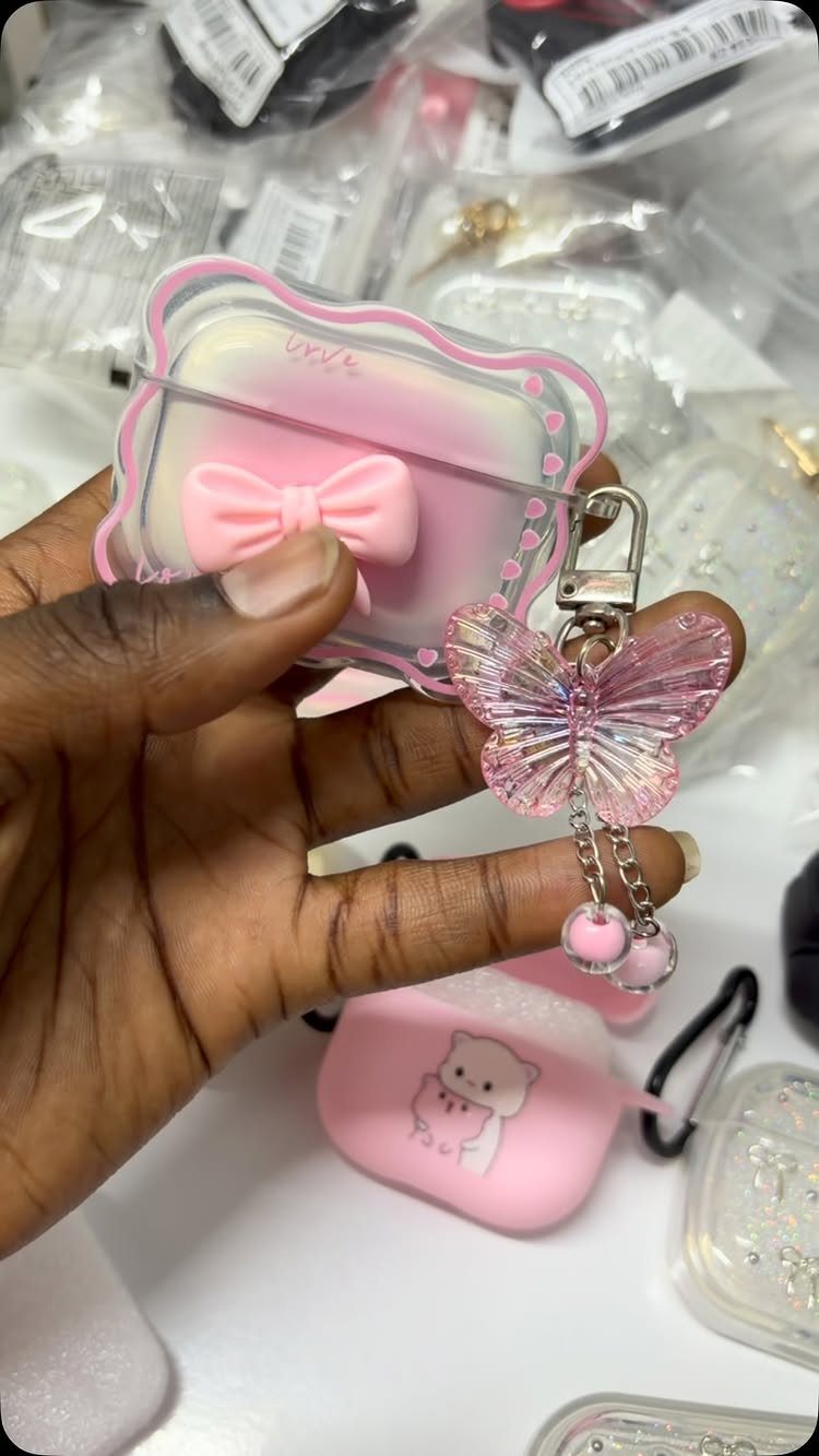 Pink and clear AirPod case with a butterfly charm held in a hand.