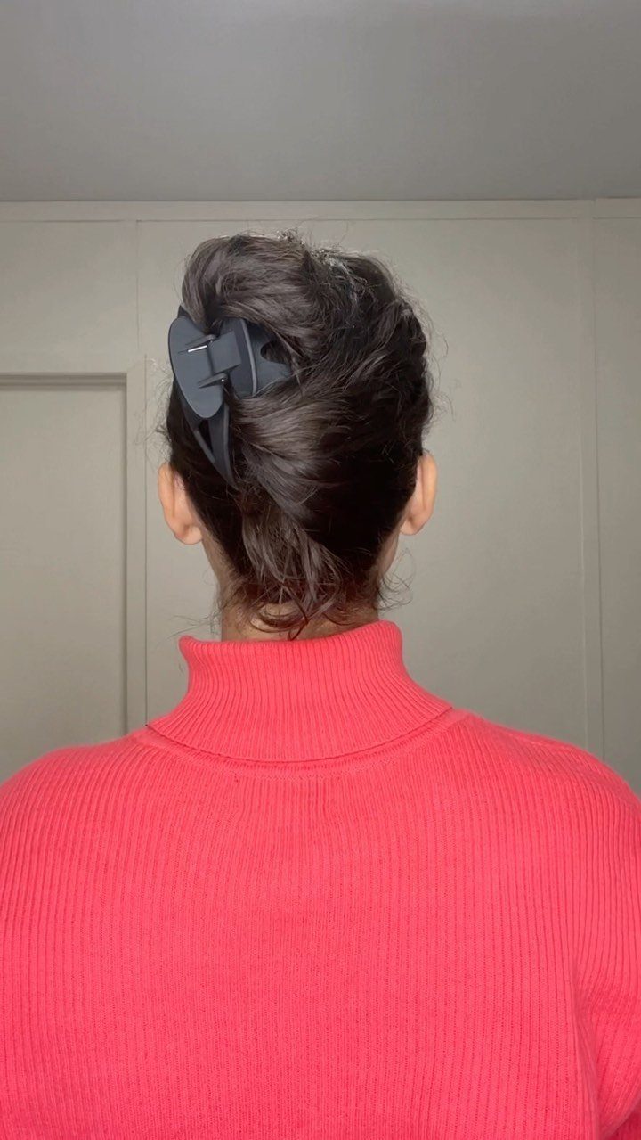 Black bow-shaped claw clip holding up brown hair on a person in red.