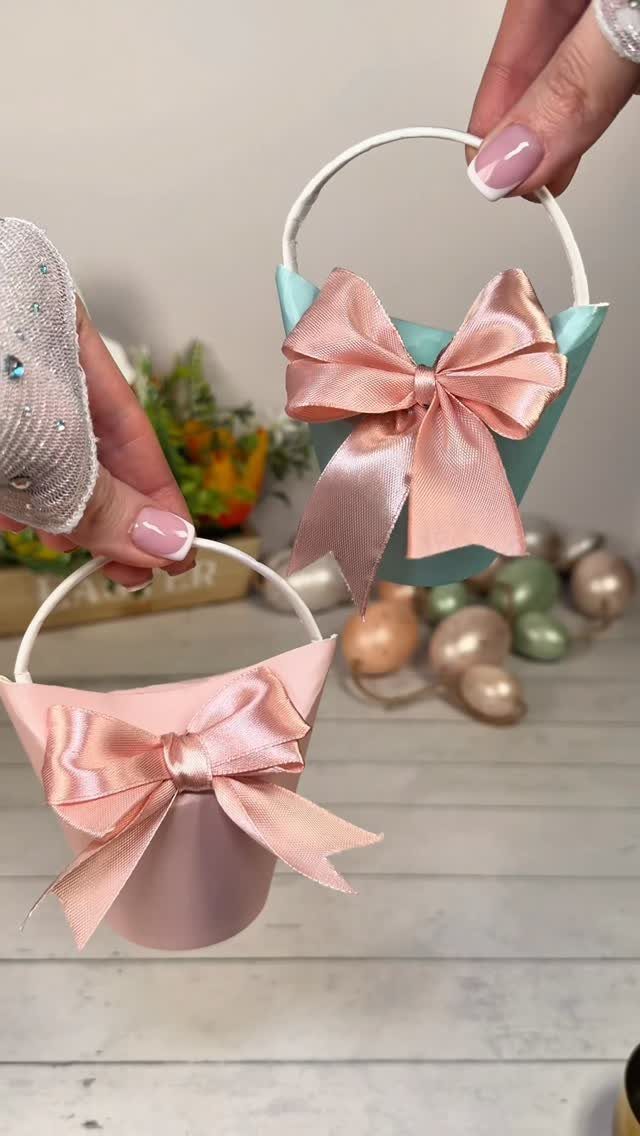 Two small cone-shaped Easter baskets with pink bows held by two hands.