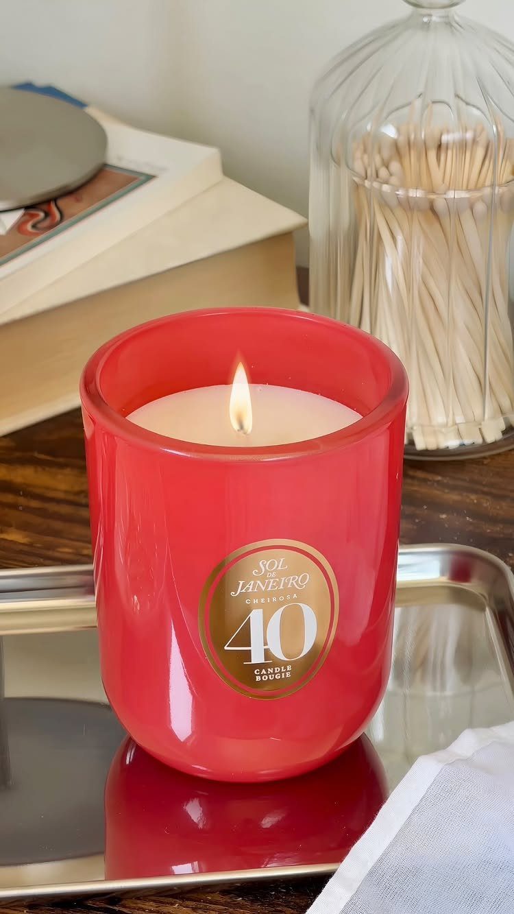 Lit scented candle in a red frosted glass jar on a silver tray.