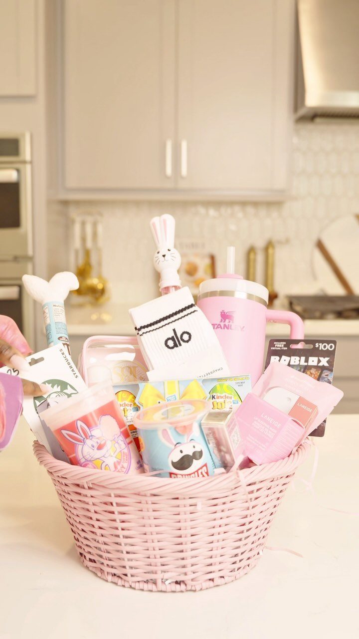 Pink wicker Easter basket filled with trendy gifts, tumbler, and candy in a kitchen.