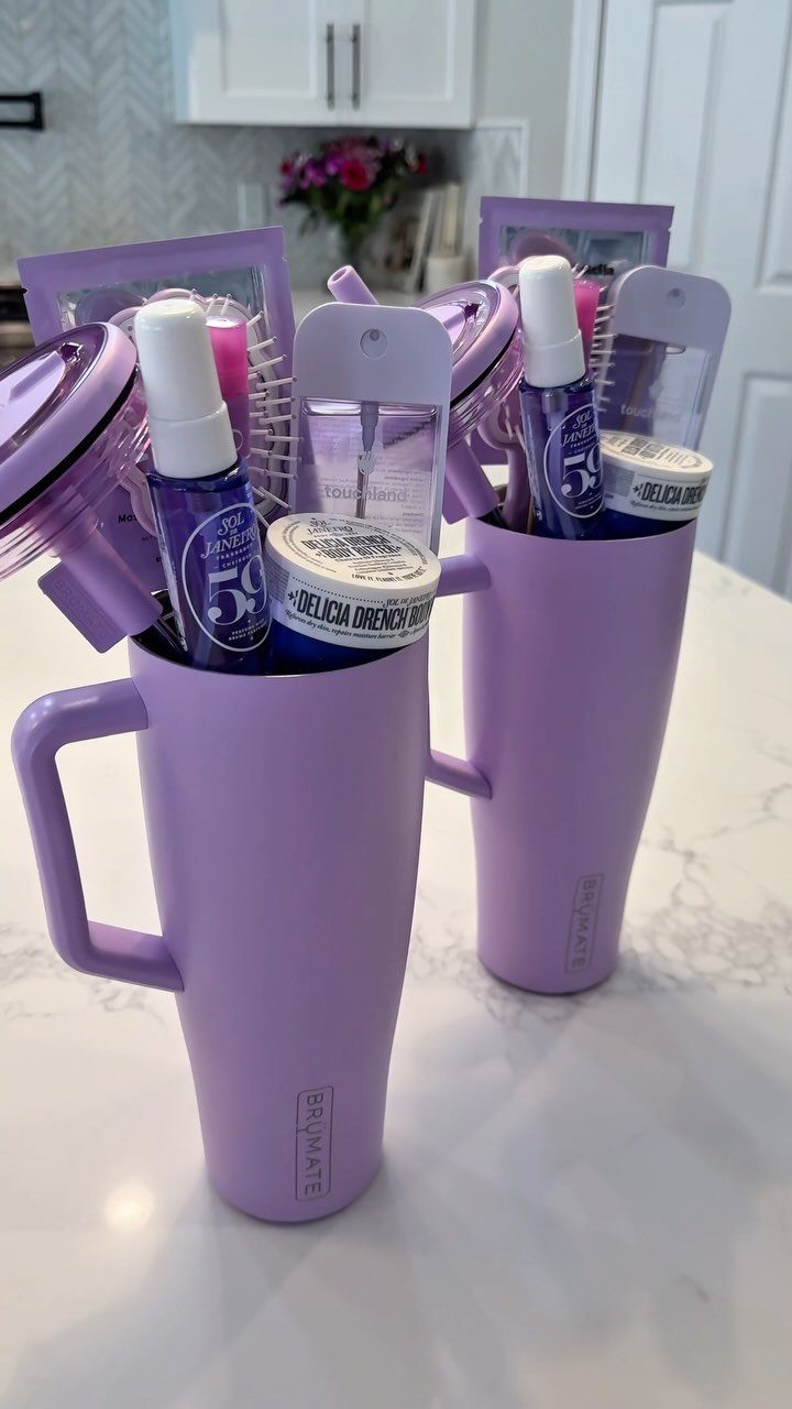 Two purple insulated tumblers filled with beauty products on a white marble counter.