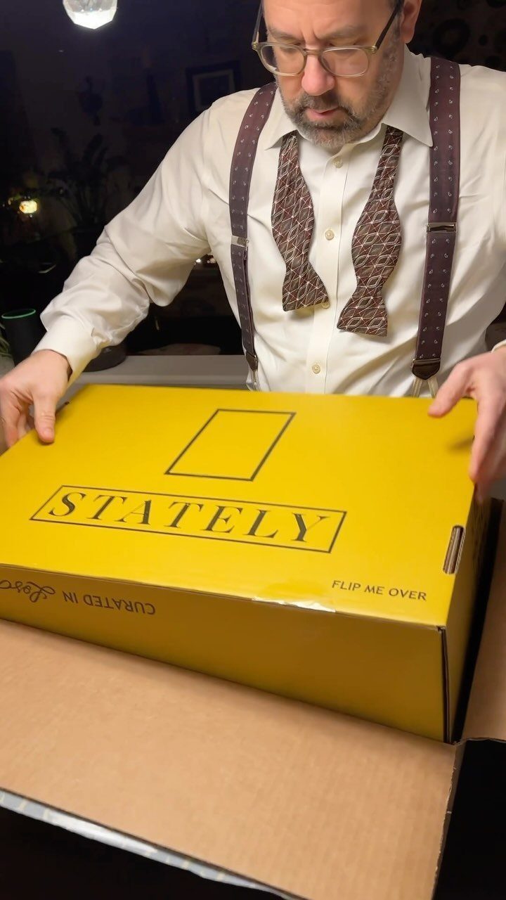 Man in bow tie and suspenders holding a yellow Stately subscription box.