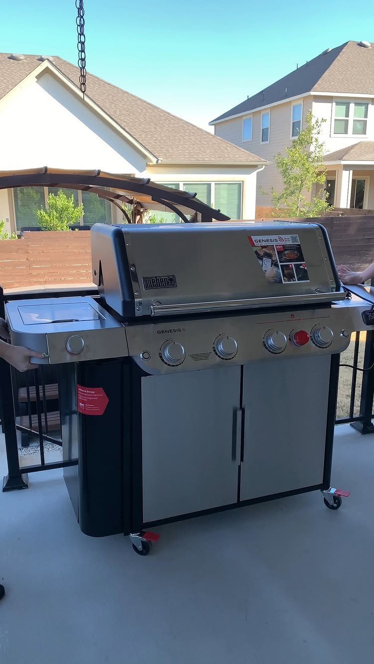 Stainless steel gas grill on a concrete patio with houses in the background