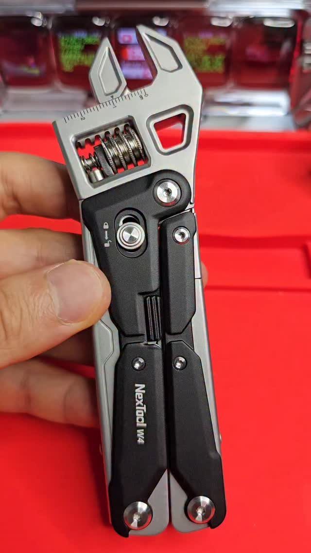 Nextool W4 pocket multitool with adjustable wrench held against a red background.