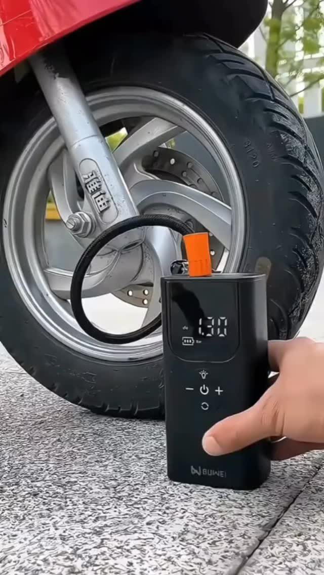 Portable electric air pump inflating a red scooter tire on a paved ground.