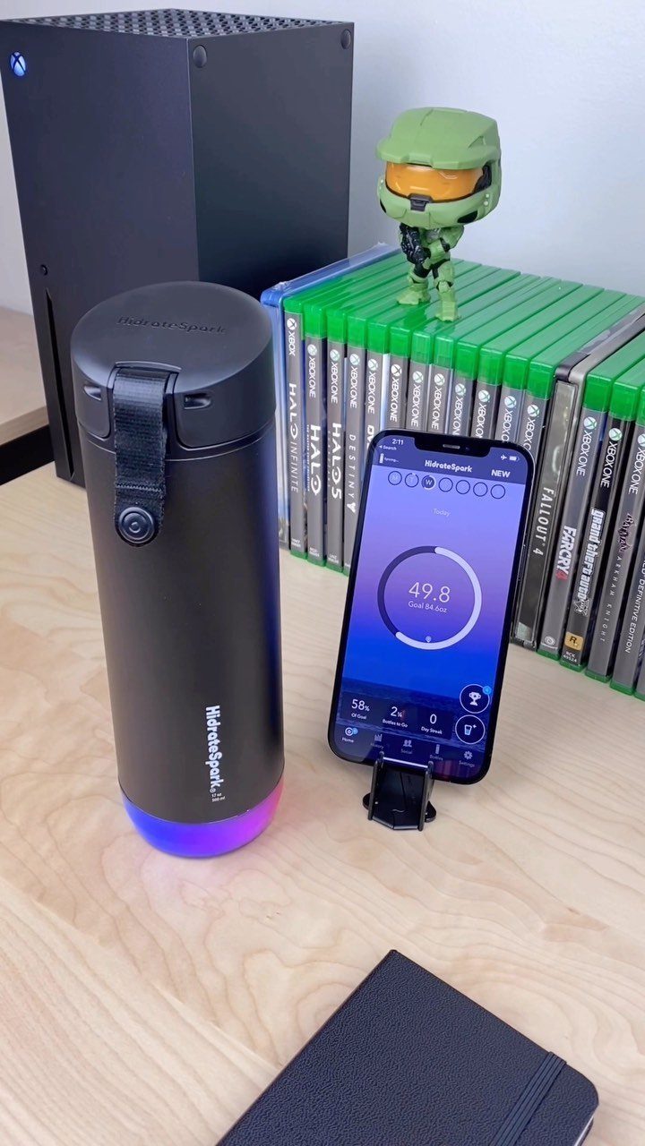Smart water bottle with glowing base next to a smartphone on wooden desk