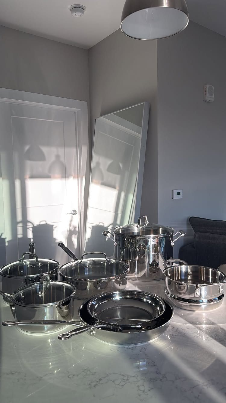 Stainless steel cookware set arranged on a white marble kitchen countertop.